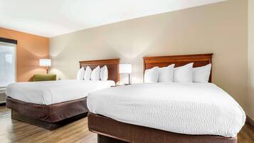 A hotel room with two beds, a green chair, and a lamp.