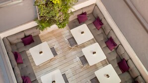 Eine Dachterrasse mit Sitzgelegenheit, weißen Tischen und einer vertikalen Begrünung.