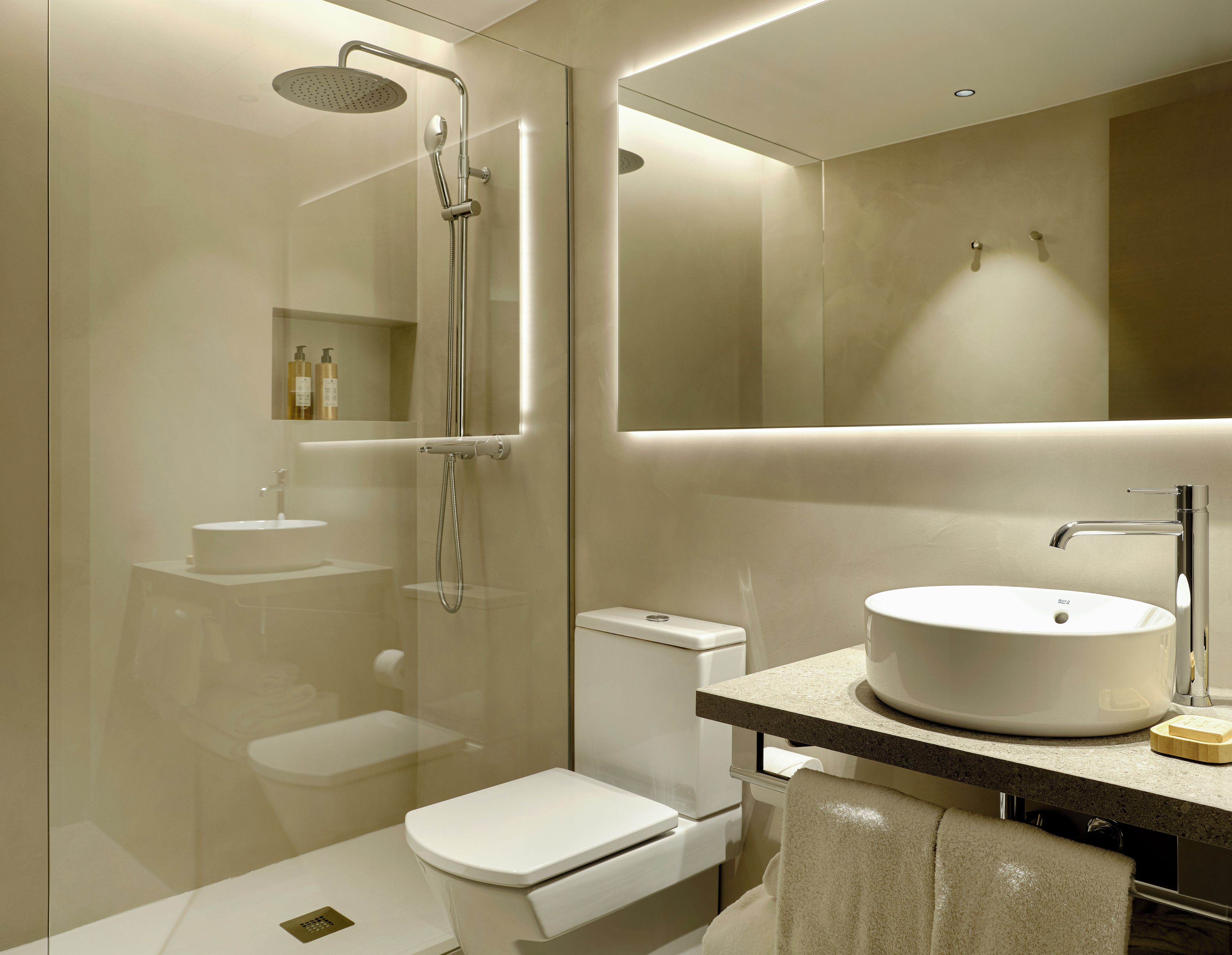 Un baño moderno con ducha de vidrio, inodoro blanco, lavamanos con cuenca redonda y espejo sobre el lavamanos.
