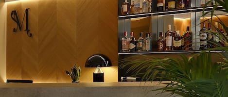 A bar area with a wooden wall, a shelf with various bottles, and two stools.