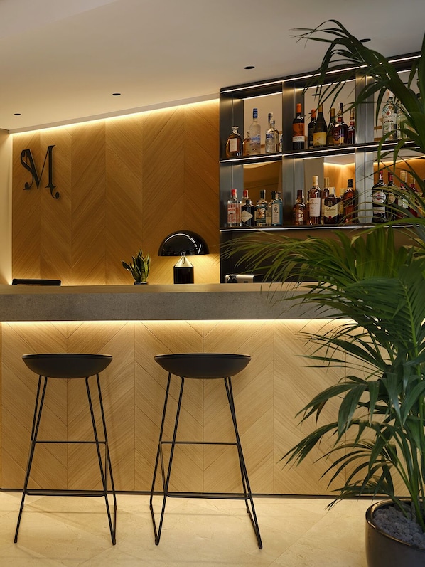 A bar area with a wooden wall, a shelf with various bottles, and two stools. - Musik Boutique Hotel - Adults Only (Barcelona)