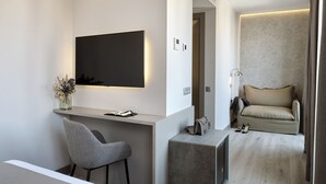 Ein modernes, minimalistisches Zimmer mit einem wandmontierten Flachbildfernseher, einem kleinen Schreibtisch mit Stuhl, einer Couch und einem Beistelltisch.
