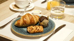 A breakfast setting with croissants, a muffin, a cup of coffee, a glass of orange juice, and a bowl of fruit on a table. - Musik Boutique Hotel - Adults Only (Barcelona)