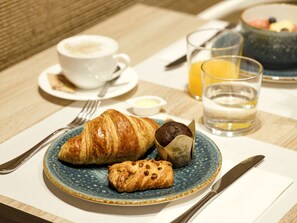A breakfast setting with croissants, a muffin, a cup of coffee, a glass of orange juice, and a bowl of fruit on a table. - Musik Boutique Hotel - Adults Only (Barcelona)