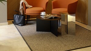 Ein modernes Zimmer mit zwei orangefarbenen Sesseln, einem schwarzen Couchtisch und einer Zeitschrift. Auf dem Boden liegt eine schwarze Handtasche.