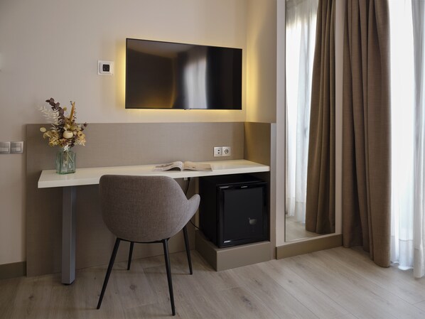 A modern hotel room with a desk, chair, flat-screen TV, and a small refrigerator. - Musik Boutique Hotel - Adults Only (Barcelona)