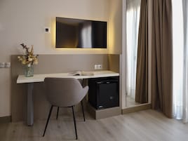 Egy modern szállodai szoba íróasztallal, székkel, síkképernyős televízióval és egy kis hűtőszekrénnyel.