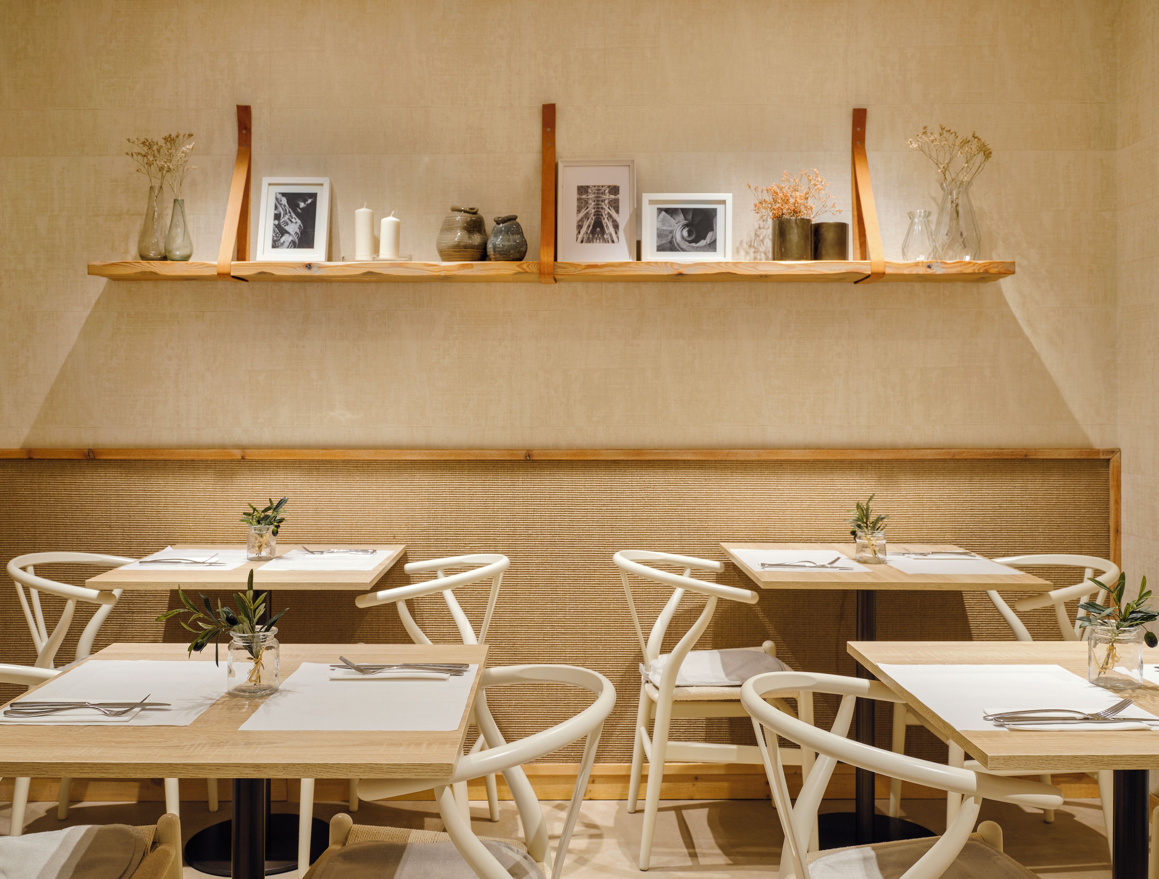Een eetgedeelte met houten tafels, witte stoelen en een wandplank met decoratieve objecten.