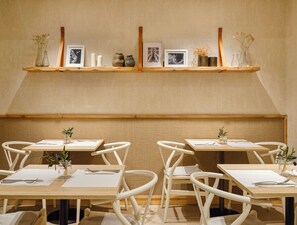 A dining area with wooden tables, white chairs, and a wall-mounted shelf with decorative items. - Musik Boutique Hotel - Adults Only (Barcelona)