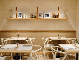 A dining area with wooden tables, white chairs, and a wall-mounted shelf with decorative items.