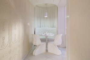 A room with a white upholstered sofa, two white chairs, a round table with a white tablecloth, and a white ceiling with a hanging light fixture. - Vice Versa (Paris)