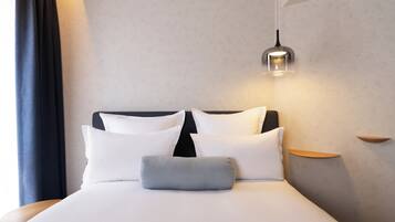 Een netjes opgemaakt bed met witte lakens en een grijs kussen, een zwart hoofdbord en een hanglamp erboven.