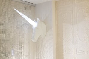 Cabeça de unicórnio branco montada numa parede texturizada, um painel decorativo com motivos florais e um teto texturizado.