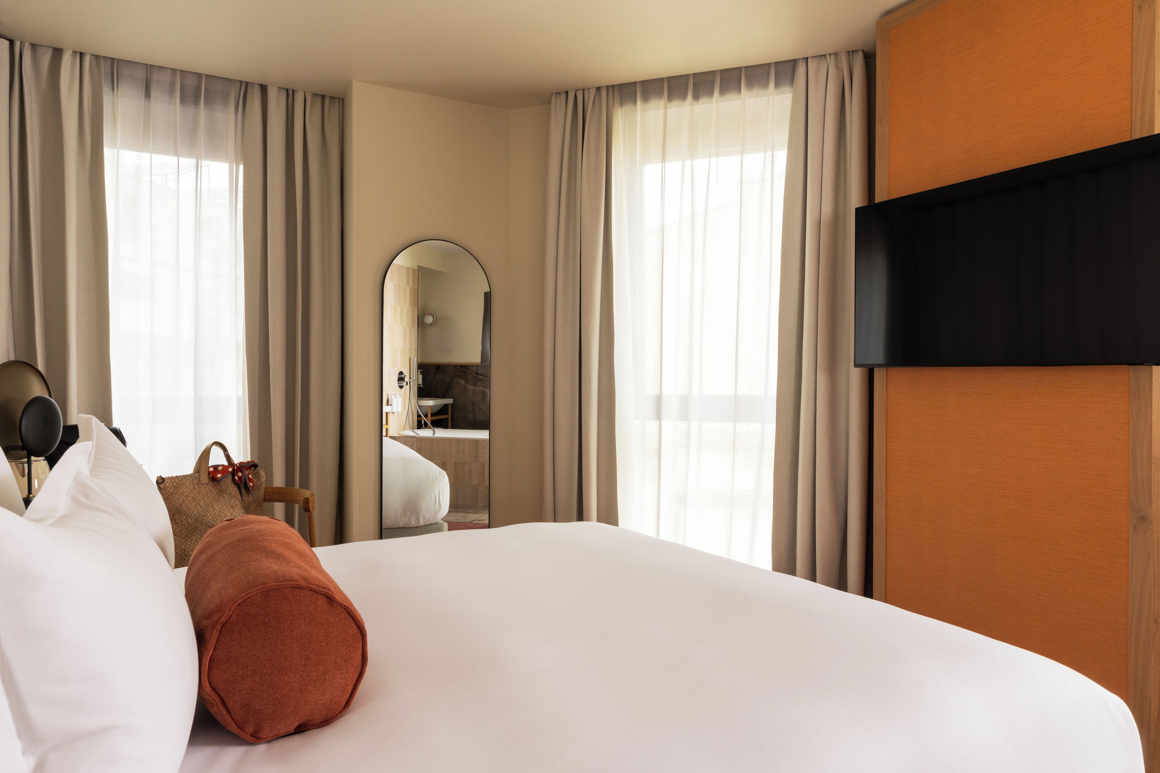 Une chambre d’hôtel avec un grand lit, un téléviseur à écran plat, un miroir et une salle de bain visible à travers une arche.