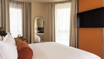 A hotel room with a large bed, a flat-screen TV, a mirror, and a bathroom visible through an archway.