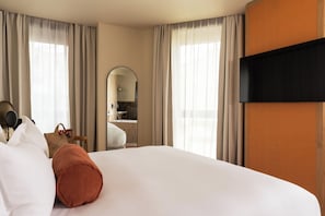 A hotel room with a large bed, a flat-screen TV, a mirror, and a bathroom visible through an archway. - Vice Versa (Paris)