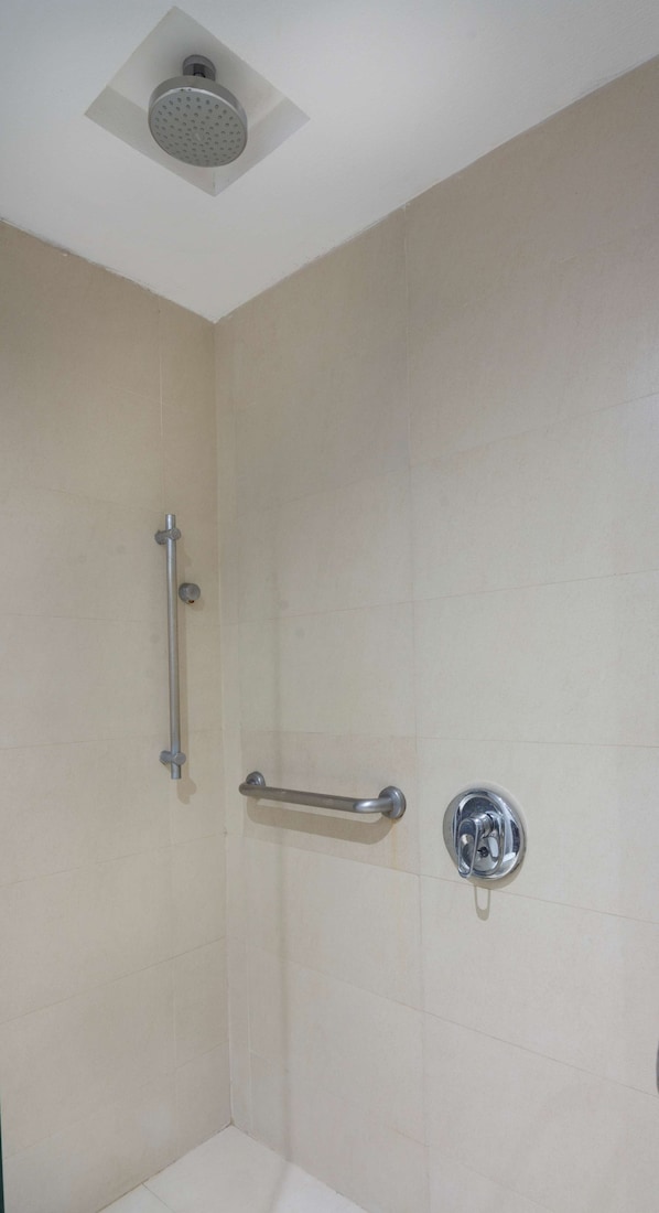 A shower area with a handheld showerhead, grab bar, and a wall-mounted faucet.