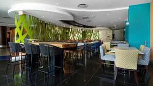 A modern restaurant with high tables and chairs, a curved ceiling, and a vibrant green wall.