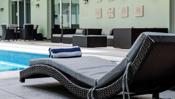 A poolside lounge area with wicker lounge chairs, a towel, and a glass-enclosed room in the background.