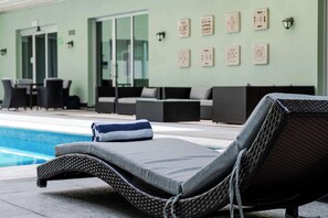 A poolside lounge area with wicker lounge chairs, a towel, and a glass-enclosed room in the background.