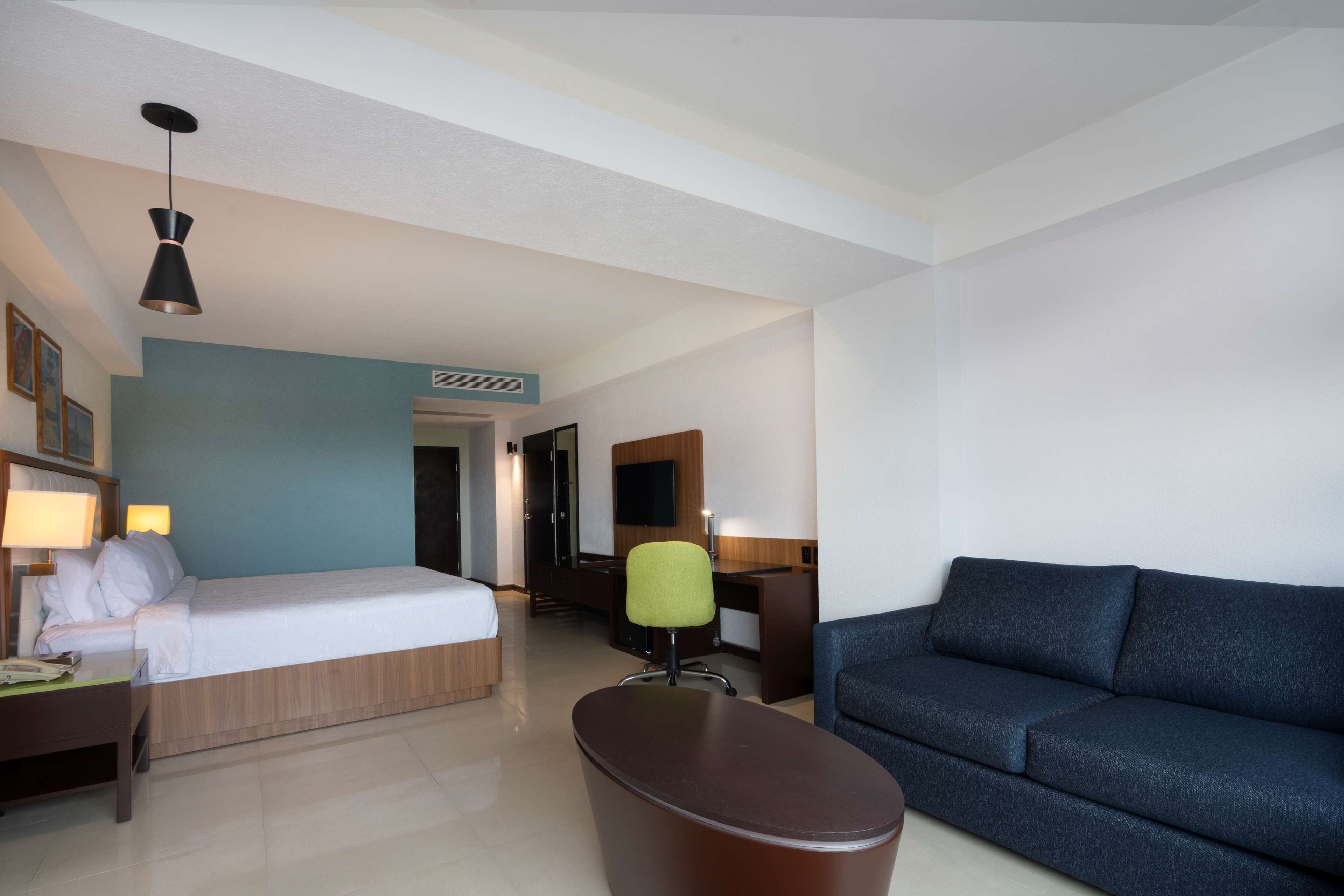 A hotel room with a bed, desk, chair, and a sofa.