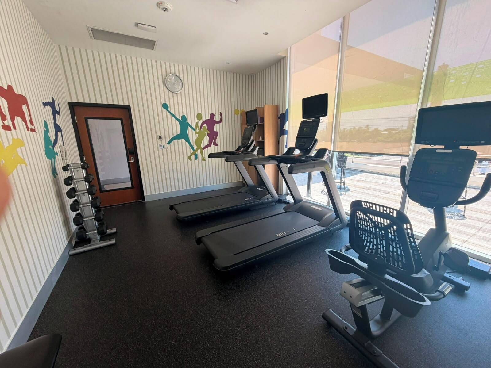 Ein Fitnessraum mit Laufbändern, einem Ergometer und einer Wand mit farbenfrohen Silhouetten.