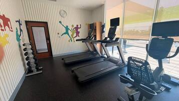 Ein Fitnessraum mit Laufbändern, einem Ergometer und einer Wand mit farbenfrohen Silhouetten.