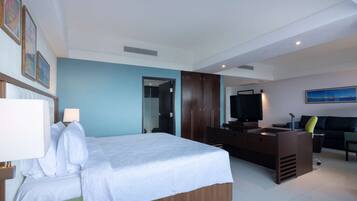 Une chambre d’hôtel moderne dotée d’un grand lit, d’un bureau avec un téléviseur à écran plat et d’un coin salon comprenant un canapé et des fauteuils.