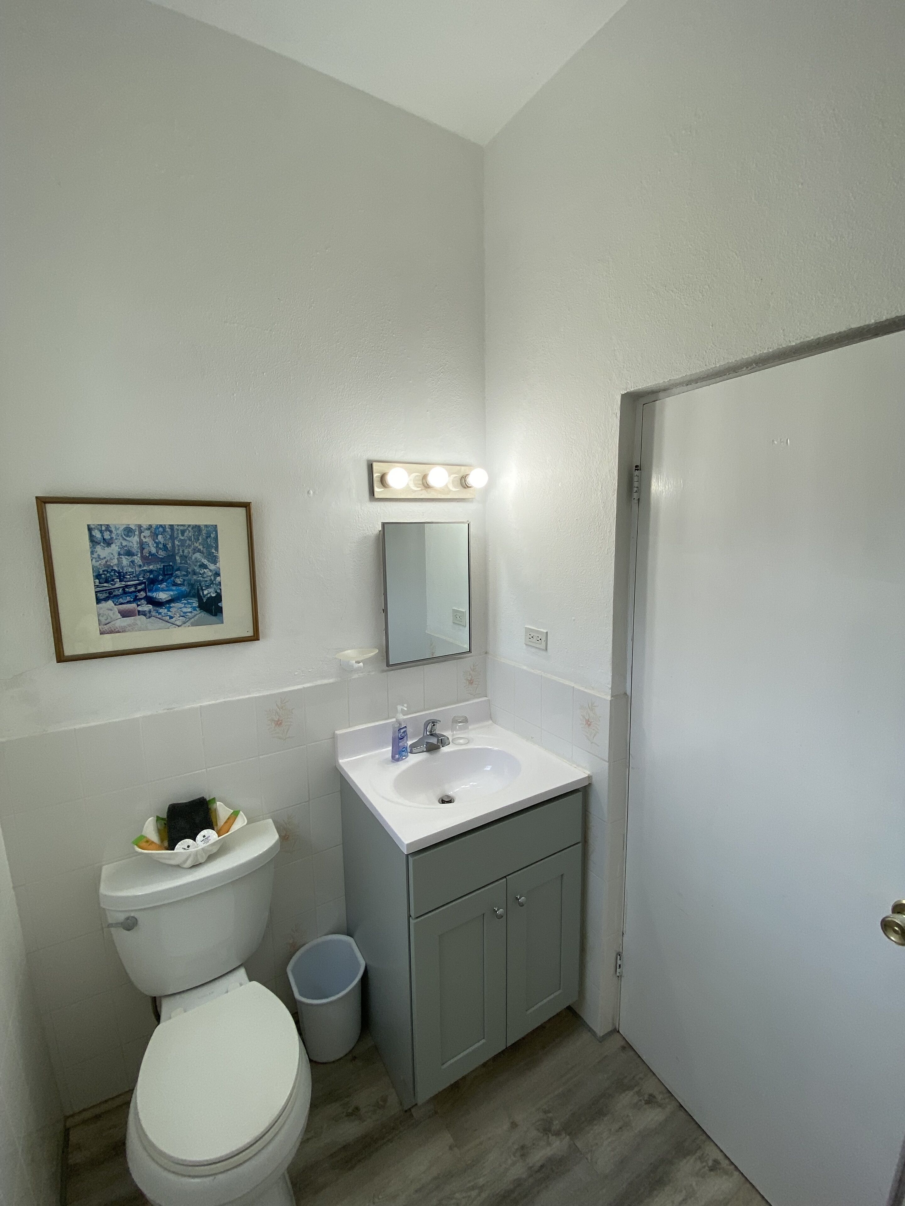 A bathroom with a toilet, sink, mirror, and a framed picture on the wall.