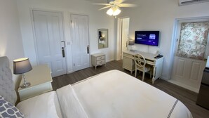 A hotel room with a bed, desk, chair, TV, and wardrobe. - Edgehill Manor Guest House (Pembroke Parish)