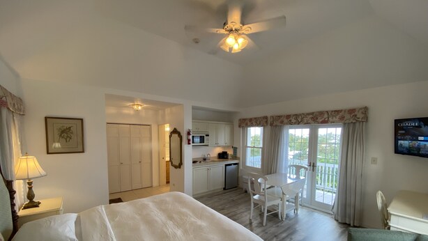 A hotel room with a bed, a desk, a chair, a television, and a balcony with curtains. - Edgehill Manor Guest House (Pembroke Parish)