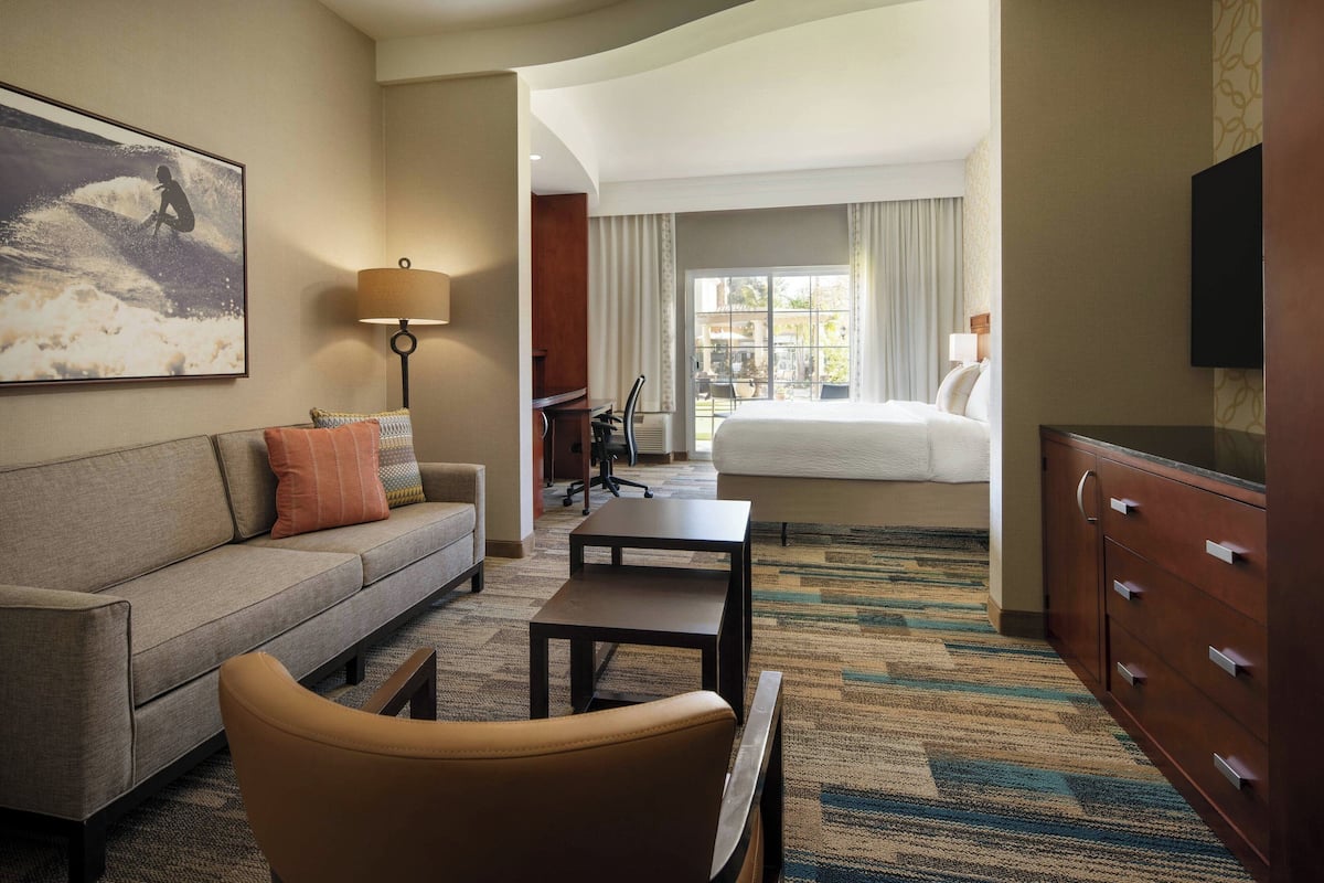 A hotel room with a sofa, armchair, desk, and dresser.