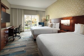 A hotel room with two beds, a desk, a chair, a TV, and a view of the outside.