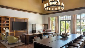 A spacious living room with a large dark wood dining table, comfortable seating, a television, and a view of the outdoors through large windows. - Courtyard Santa Barbara Goleta (Goleta)