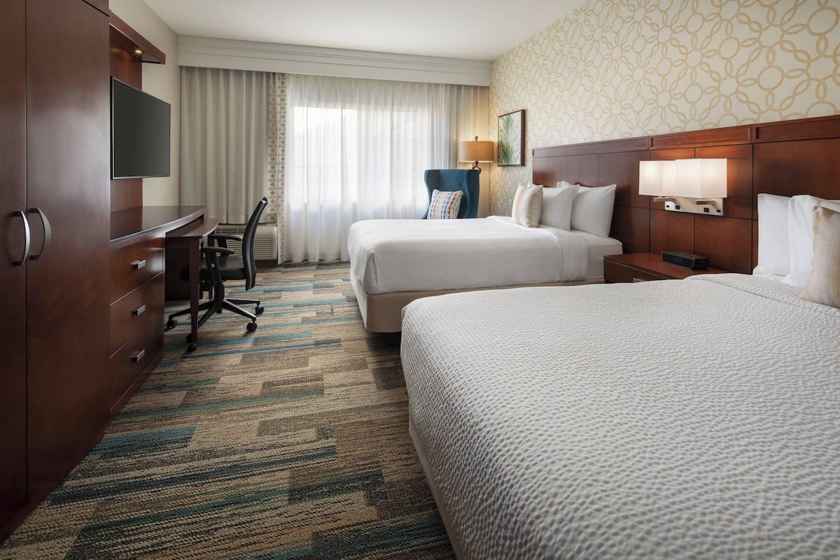 A hotel room with two beds, a desk, a TV, and a lamp.
