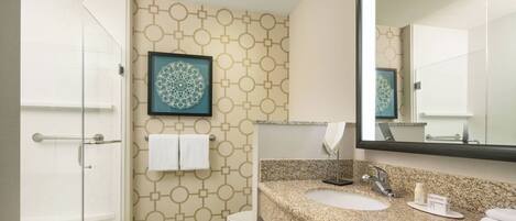 A modern bathroom with a glass shower enclosure, a sink with a granite countertop, and a toilet.