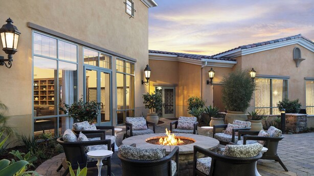 An outdoor patio with wicker furniture, a central fire pit, and potted plants. - Courtyard Santa Barbara Goleta (Goleta)