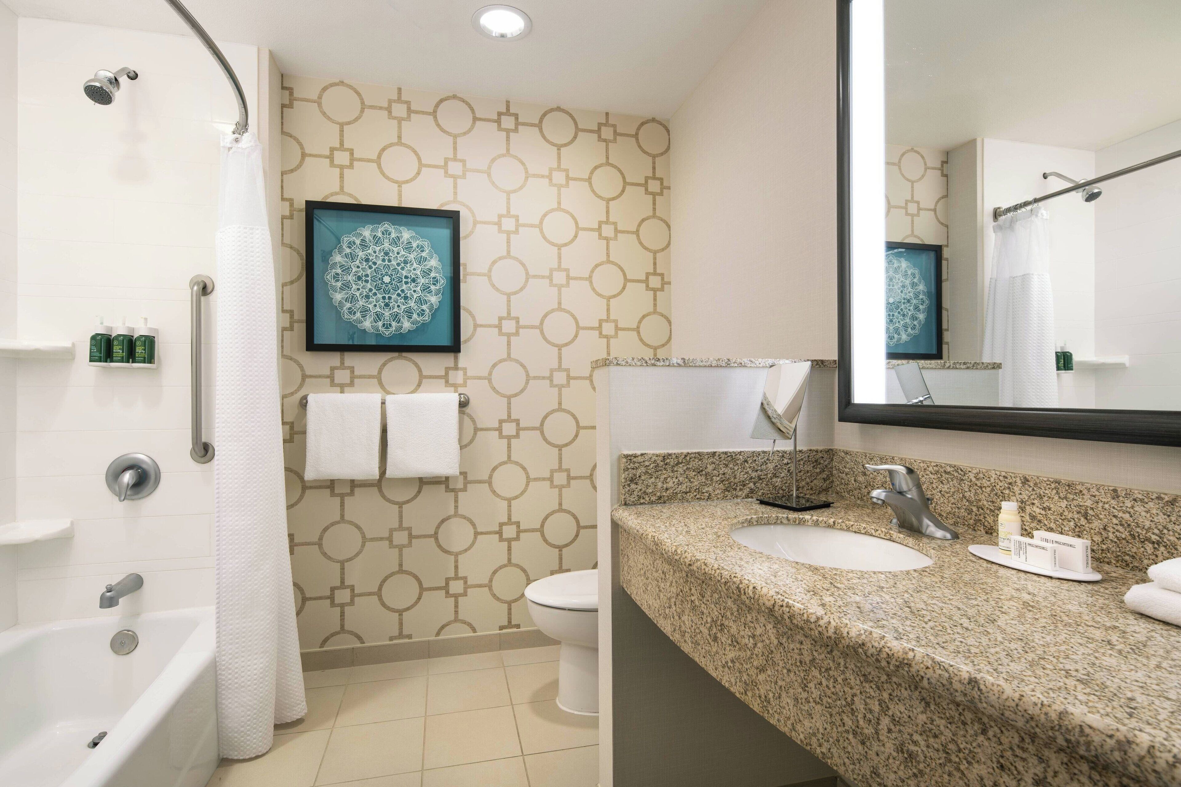 A bathroom with a shower, toilet, sink, and a large mirror.