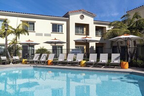 A swimming pool with lounge chairs and umbrellas, a sign prohibiting diving, and a building with a tiled roof and balconies.