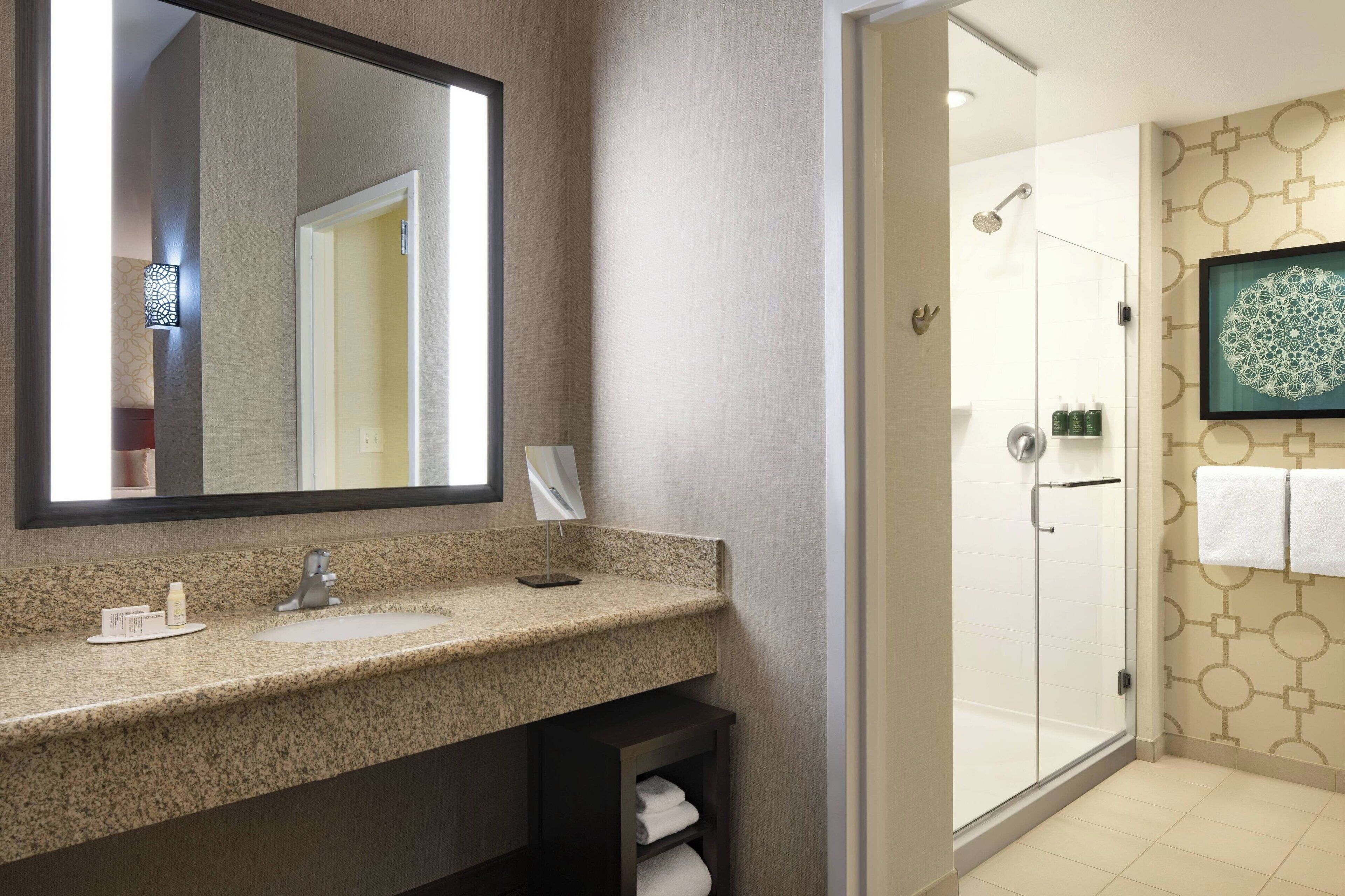 A bathroom with a granite countertop sink, a large mirror, a glass shower enclosure, and a wall-mounted towel rack.