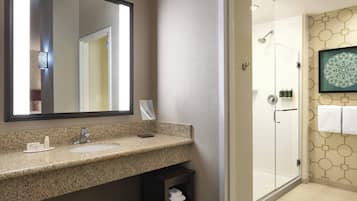 A bathroom with a granite countertop sink, a large mirror, a glass shower enclosure, and a wall-mounted towel rack.