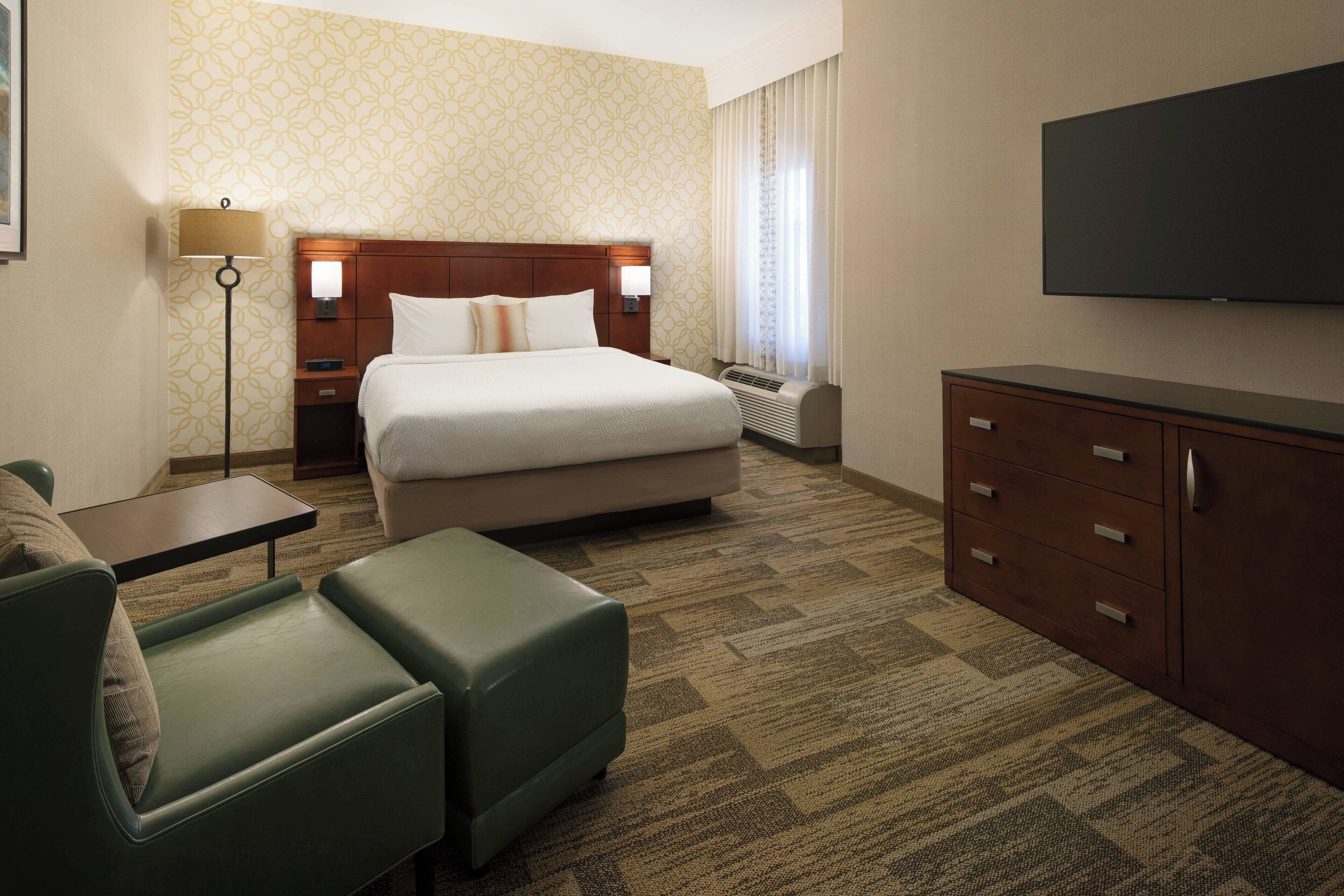 A hotel room with a large bed, a desk, a chair, a TV, and a dresser.