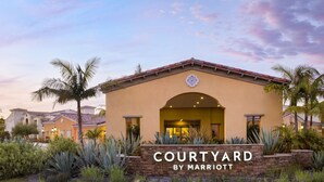 A hotel entrance with a sign reading "COURTYARD BY MARRIOTT," surrounded by landscaped greenery and palm trees. - Courtyard Santa Barbara Goleta (Goleta)