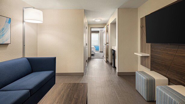 A hotel hallway with a sofa, a lamp, a TV, and a view into a bedroom. - Holiday Inn Express Richmond by IHG (Richmond)