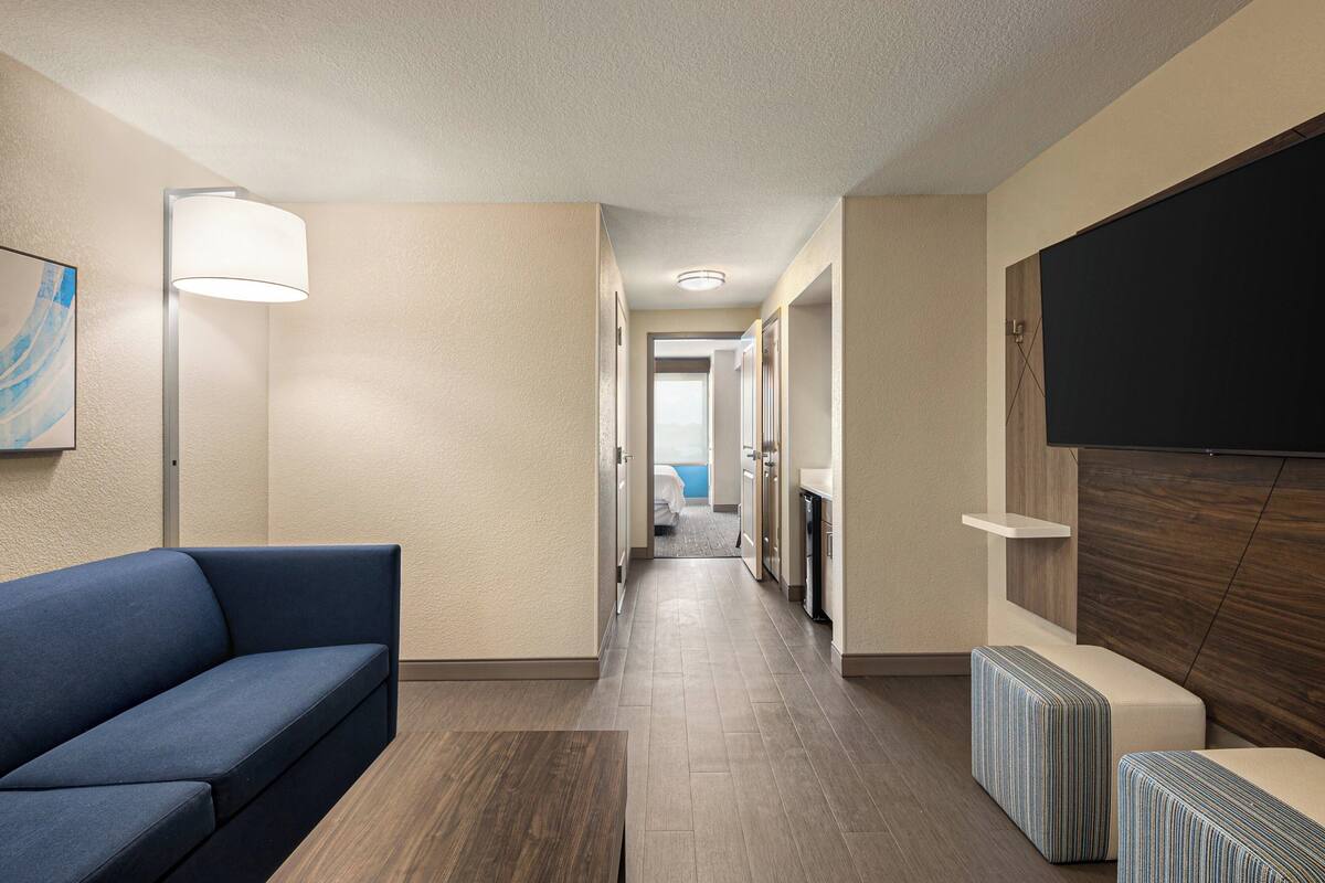 A hotel hallway with a sofa, a lamp, a TV, and a view into a bedroom.