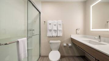 Een moderne badkamer met een douchecabine van glas, een wit toilet, een wastafel met spiegel, en handdoeken aan de muur.