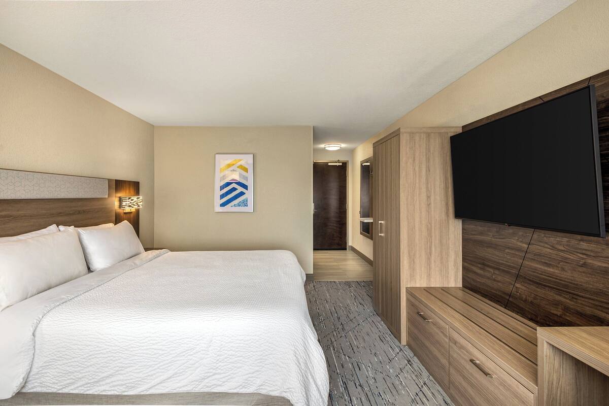 A hotel room with a large bed, a flat-screen TV, a wooden wardrobe, and a framed artwork on the wall.