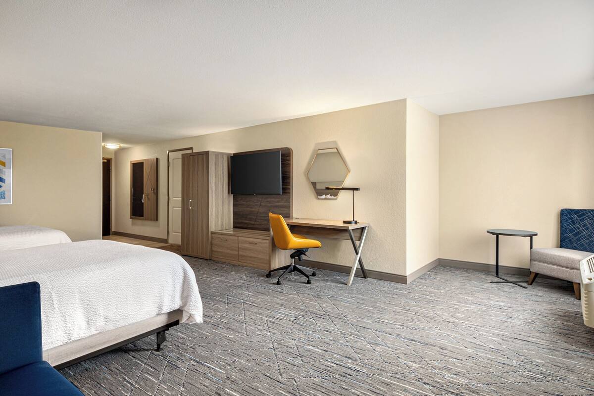 A hotel room with a bed, a desk with a chair, a TV, and a small table.