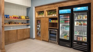 A snack bar with shelves of chips and snacks, a refrigerated section with drinks and food, and a display of bottled water. - Holiday Inn Express Richmond by IHG (Richmond)