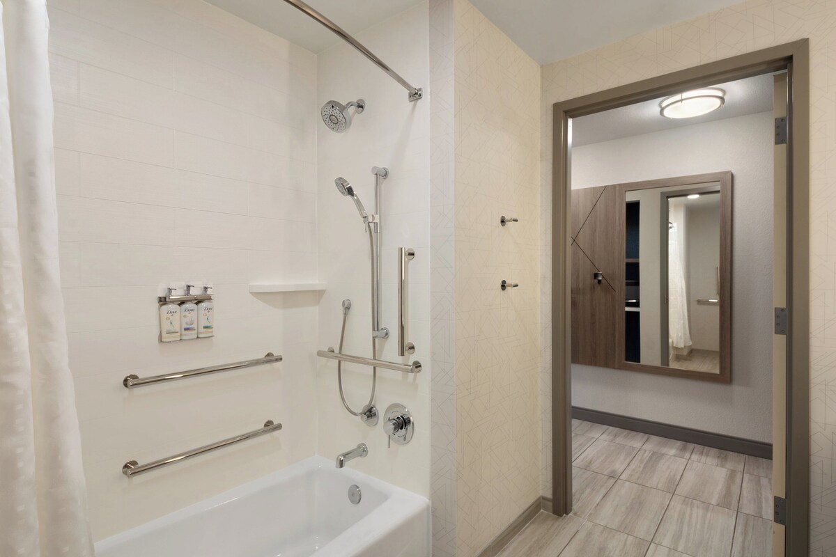 A modern bathroom with a bathtub, shower, and handrails.
